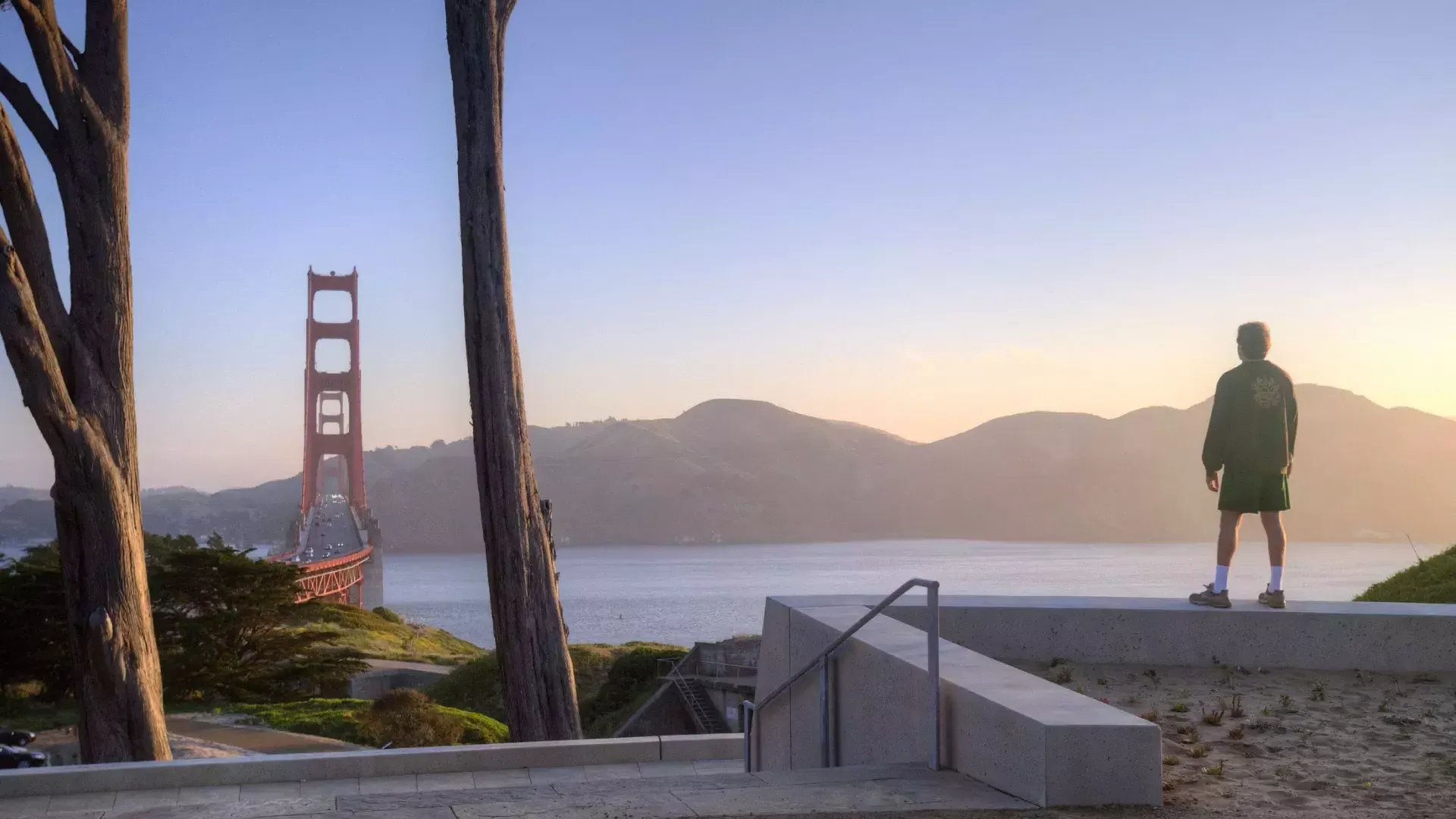 A man overlooks the Golden Gate Bridge with mountains in the background.